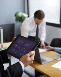 Profesional usando una tableta con gráficos junto a un equipo, simbolizando análisis gráficos y simplificación de datos para la toma de decisiones empresariales