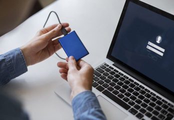 Persona conectando un dispositivo externo a una computadora portátil con pantalla de inicio de sesión, simbolizando soluciones personalizadas de gestión de identidades y accesos (IAM). Protección Integral