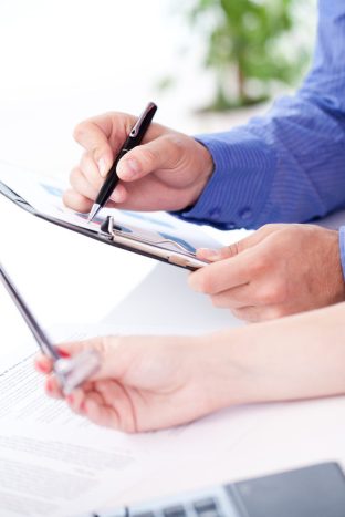 Manos colaborando sobre documentos, simbolizando la adaptación a normativas y estándares específicos durante el desarrollo de software. Protección Integral