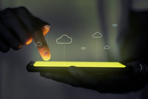 Dedo interactuando con dispositivo móvil, mostrando iconos de nubes y conectividad IoT, simbolizando ventajas de la nube con actualizaciones OTA seguras